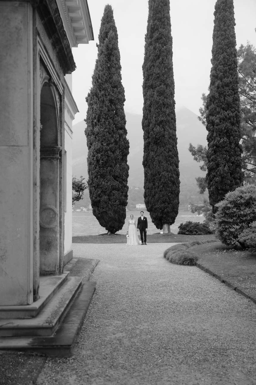 Bride and groom standing between two large cypress trees during their wedding shoot at Villa Melzi Garden, Lake Como, Italy.