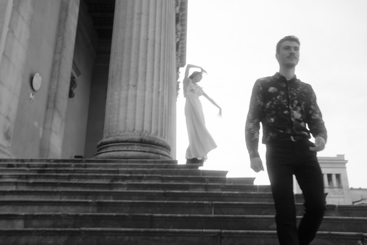 Bride dancing behind her groom on an antique staircase near Königsplatz in Munich, capturing a playful and romantic moment.