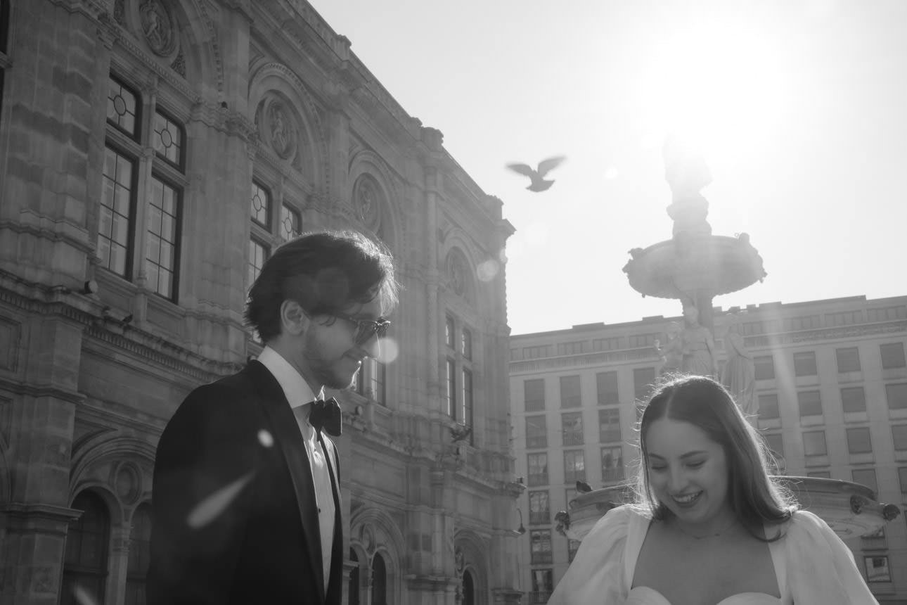 Bride and groom stand in front of the Vienna Opera during their wedding shoot as a dove flies by.
