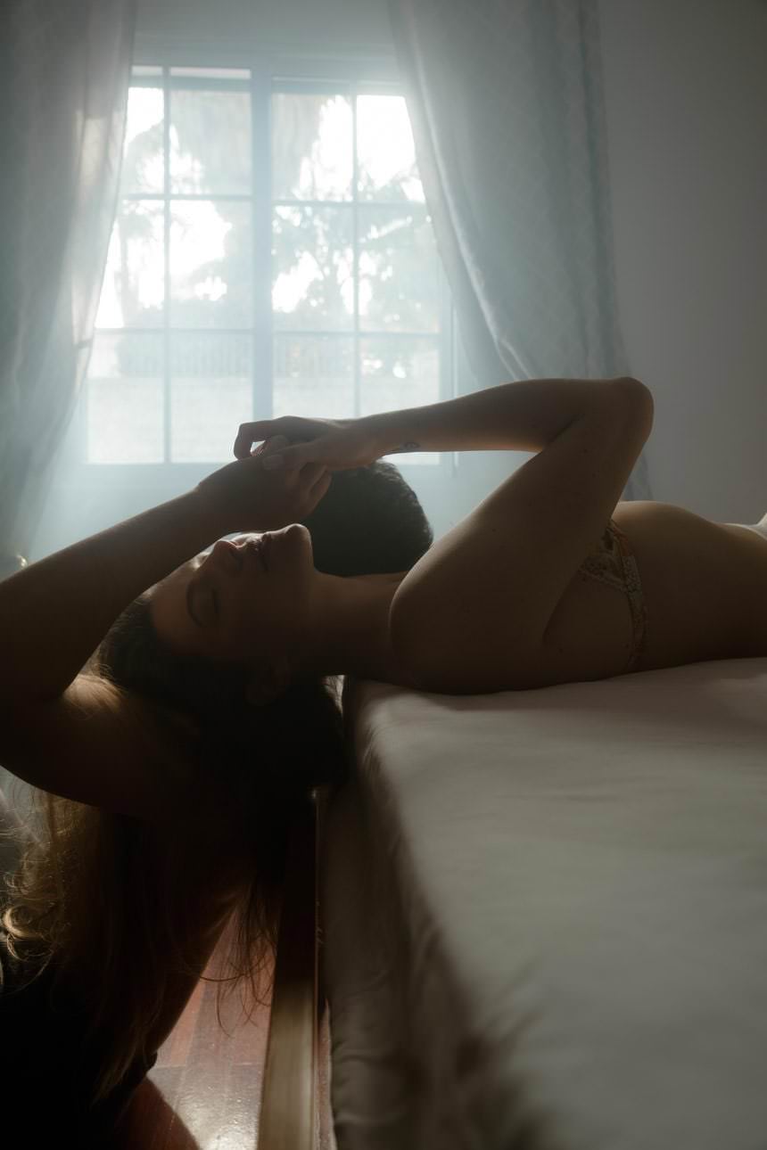 Couple holding hands on the bed during a photoshoot, bathed in beautiful light, creating an intimate and warm atmosphere.