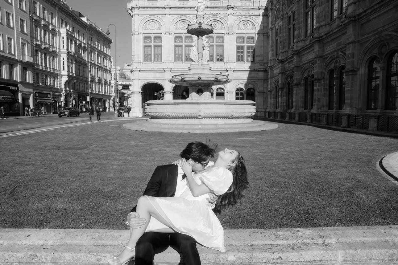 Groom kisses his bride right after their wedding in front of a fountain near the Vienna Opera House.