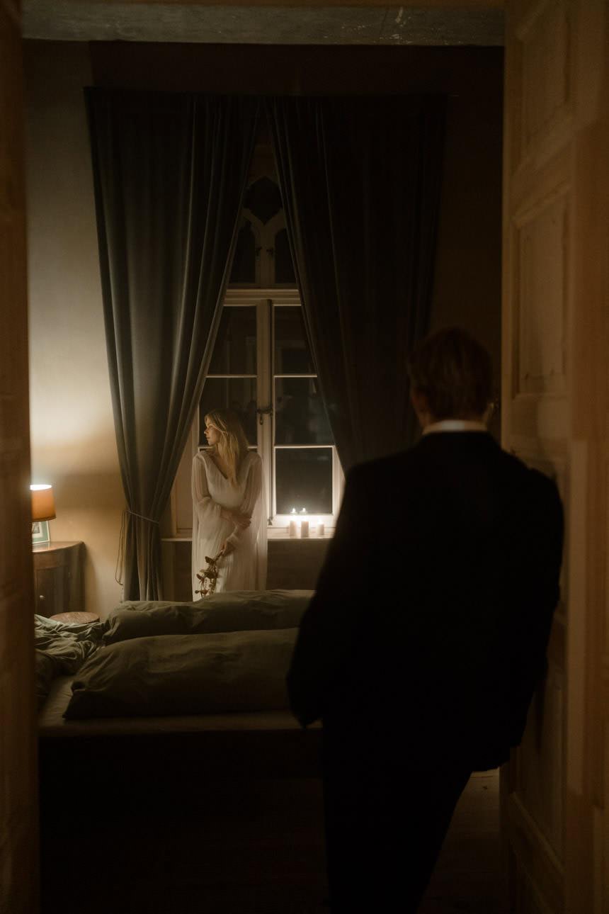 Groom standing at the door of a chateau bedroom near Paris, France, looking at his bride in a cinematic wedding scene.