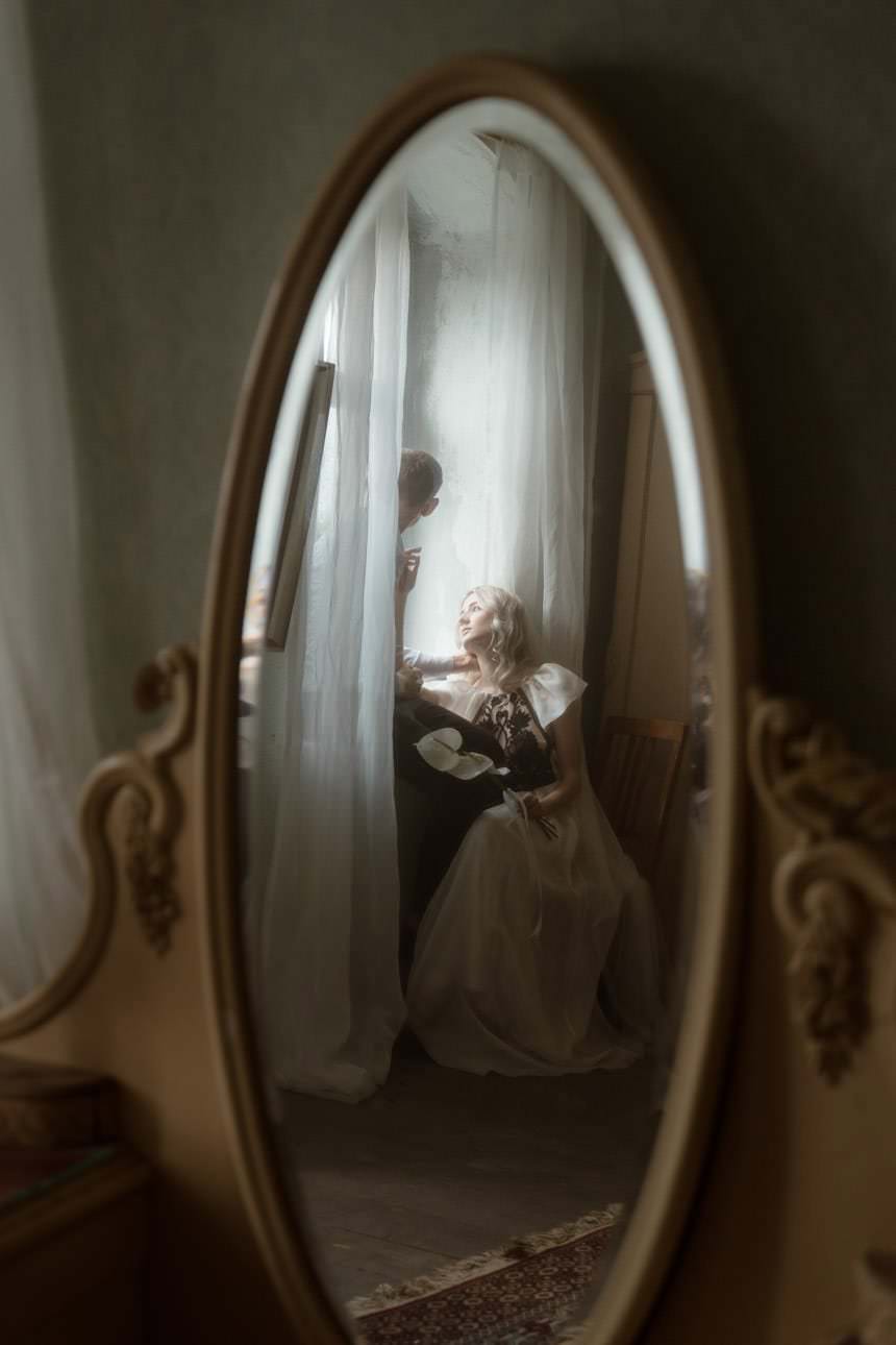 Wedding couple reflected in an antique mirror during a cinematic scene, capturing a timeless and romantic moment.